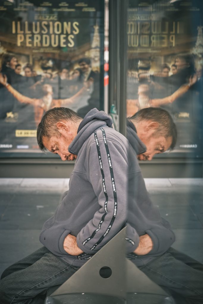 Homme endormi sous un abribus en avant plan d'une affiche